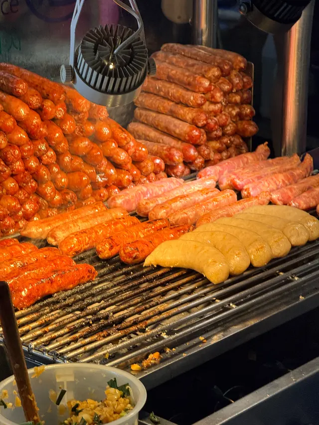 Photographed at Shilin Night Market in Taipei, where rows of sausages in different flavors cover the grill as a small fan pushes the heat aside.