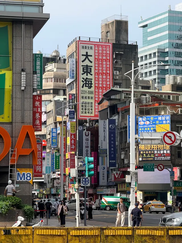 Photographed near Exit M8 of Taipei Main Station, where dense shop and cram-school signs cover older facades above the traffic and pedestrians at the junction.