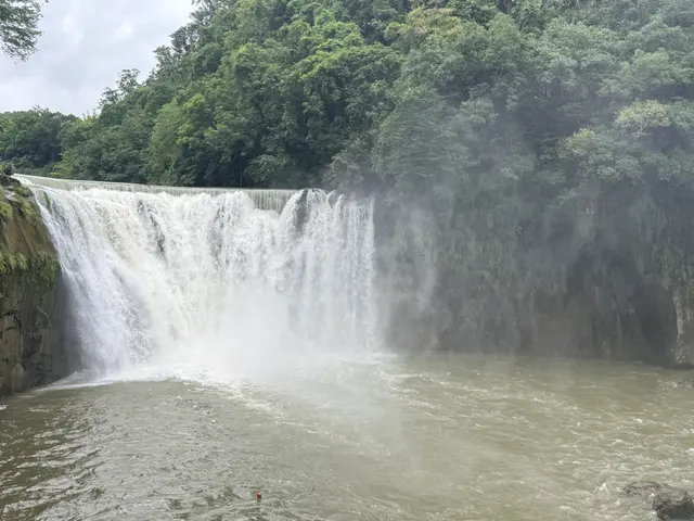 Photographed at Shifen Waterfall in New Taipei, where a broad curtain of water drops over the rock face and rising spray veils the forest beside it.