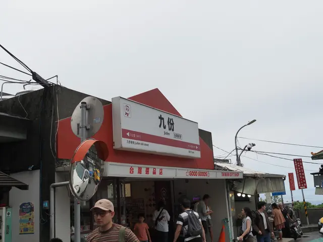 Photographed at the entrance to Jiufen Old Street in New Taipei, where the red-and-white sign stands among shops and passing visitors as the hillside town rises beyond.