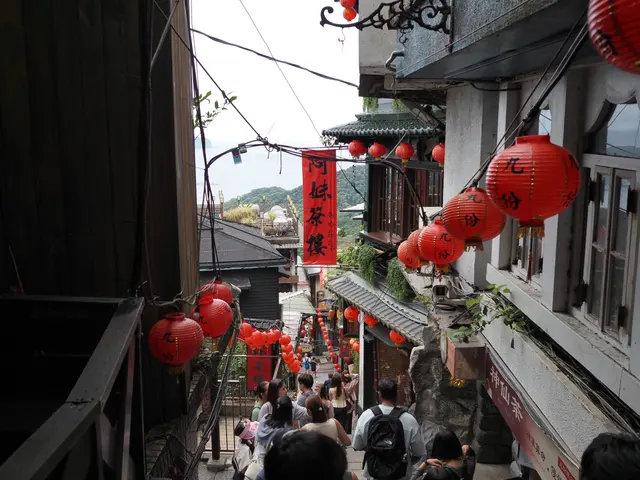 Photographed in Jiufen, New Taipei, where red lanterns descend a steep stairway between teahouses and tiled roofs, with a glimpse of the sea beyond the narrow lane.