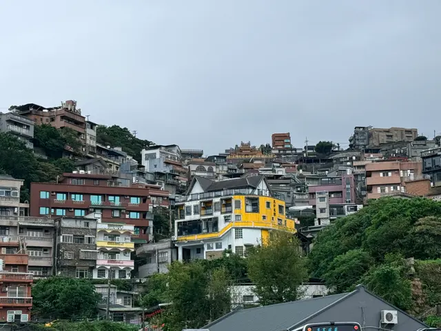 Photographed in Jiufen, New Taipei, where tightly packed homes climb the hillside and a temple roof and vivid yellow building emerge from the gray-green townscape.
