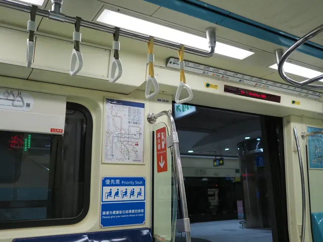 Photographed inside a Taipei Metro carriage, where the sign points toward Xindian and empty hand straps hang above the open doors and platform lights.