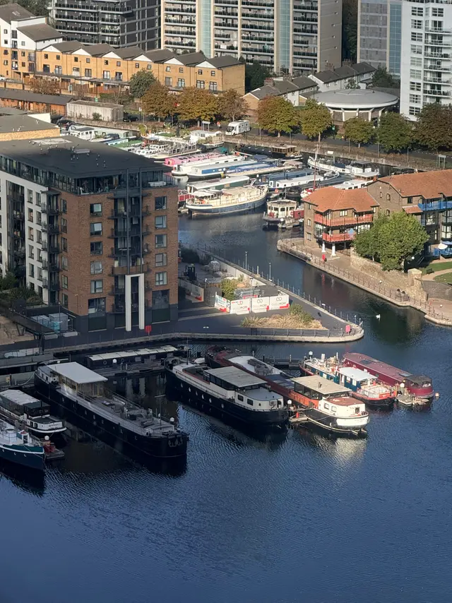 At Blackwall Basin in London, moored boats sit beside brick homes and taller apartment blocks, with afternoon sunlight catching their hulls and fine ripples across the water.